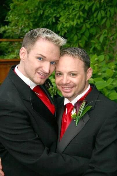 a young Jacob & Steve in black jackets and red ties, a lilac bush in the background