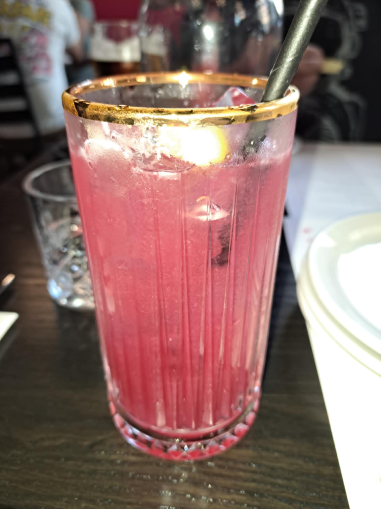 Pink frosty drink in a gold rimmed tumbler with black paper straw