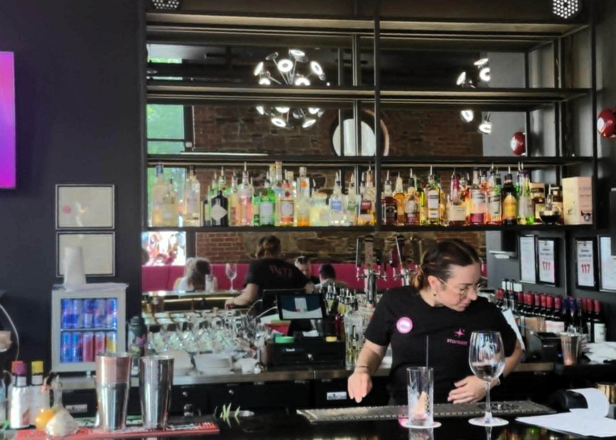 bartender at bar, shelves full of liquor bottles behind them, and a mirror behind that