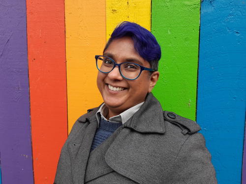 woman with glasses in front of rainbow wall