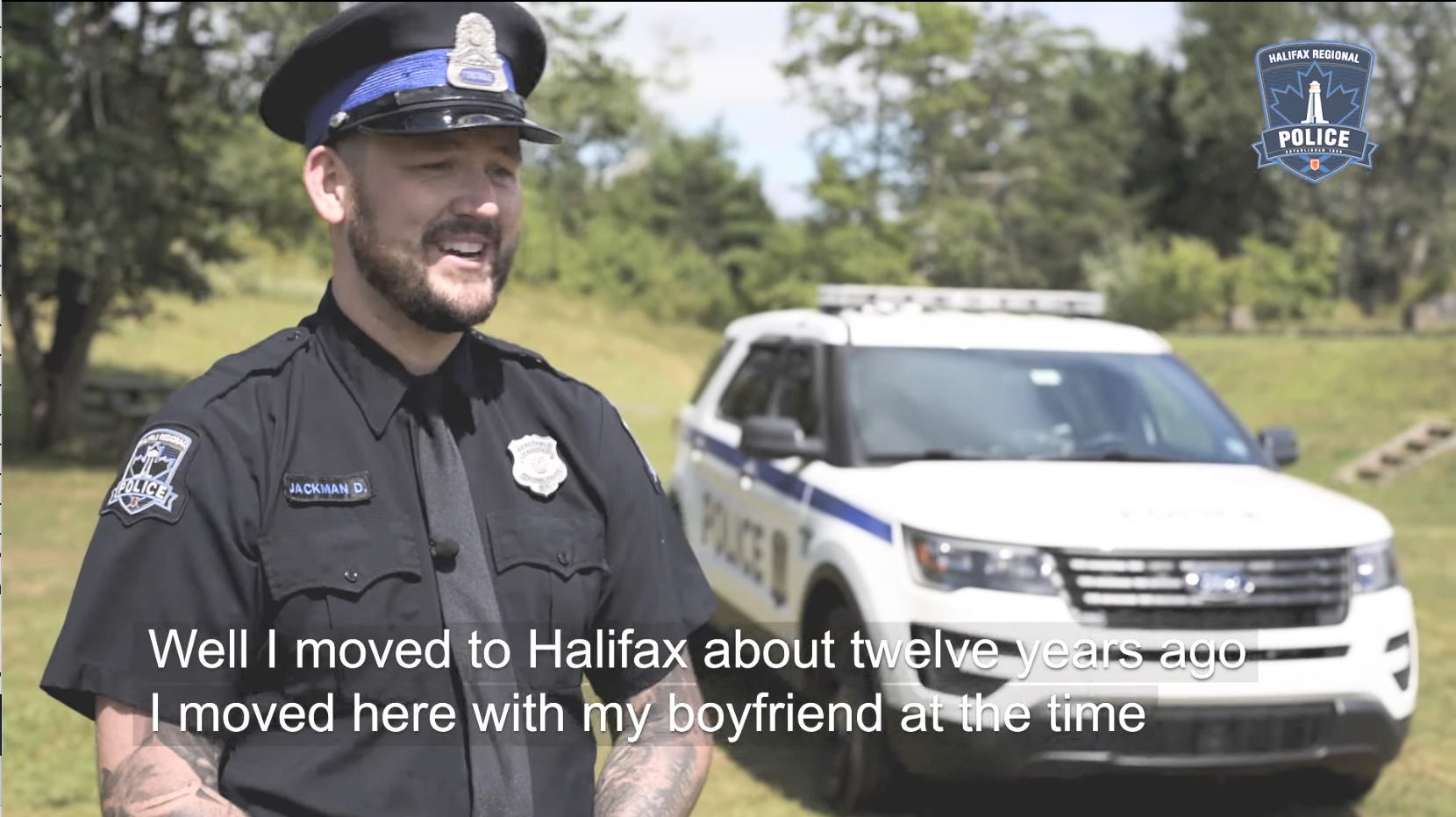 Young bearded police officer in a park, with cop car in background