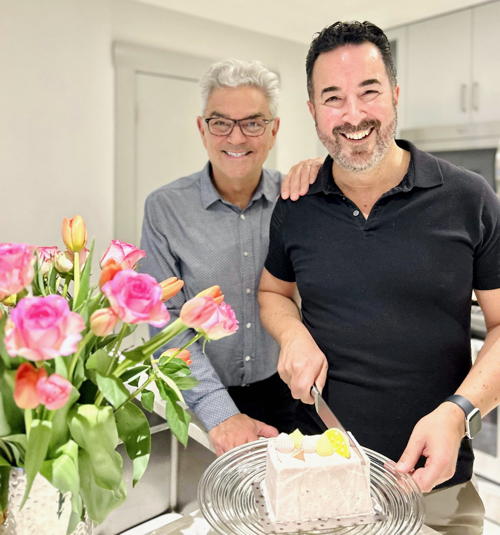 Massad and partner cutting a cake in the kitchen, vase of flowers on the table