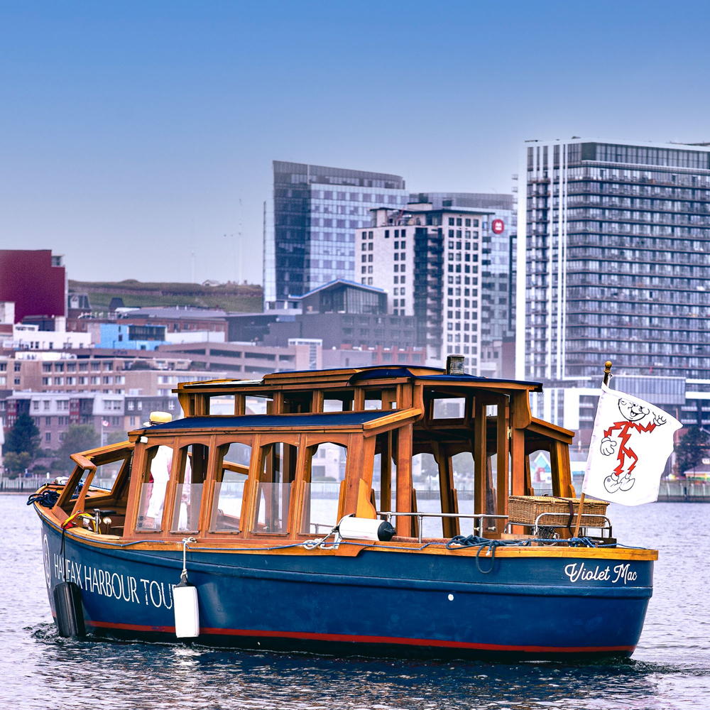 Wooden boat with Halifax skyline behind flying the "Reddy Kilowatt" flag