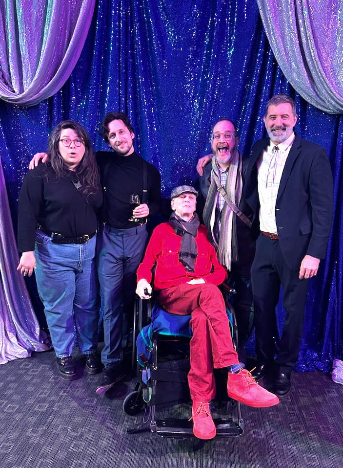 Hugo looking serene in a wheelchair surrounded by happy people