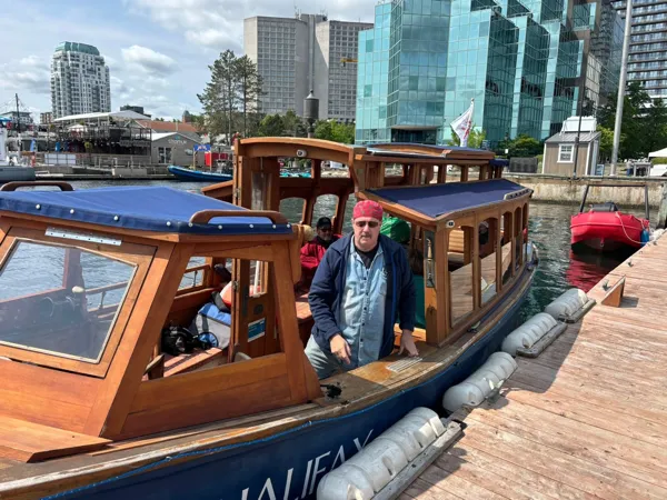 Wooden boat with Halifax skyline behind flying the "Reddy Kilowatt" flag