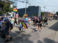 Pride parade - about 30 people, a couple carrying flags. CIBC bank building on the other side of the street.